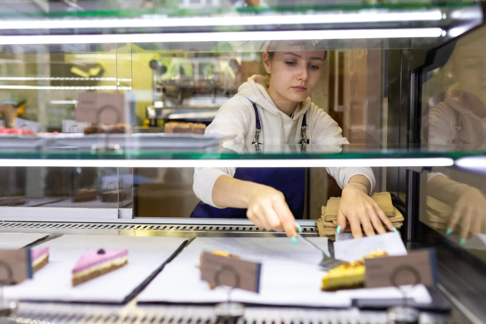 A young woman in uniform reaching into a bakery display case