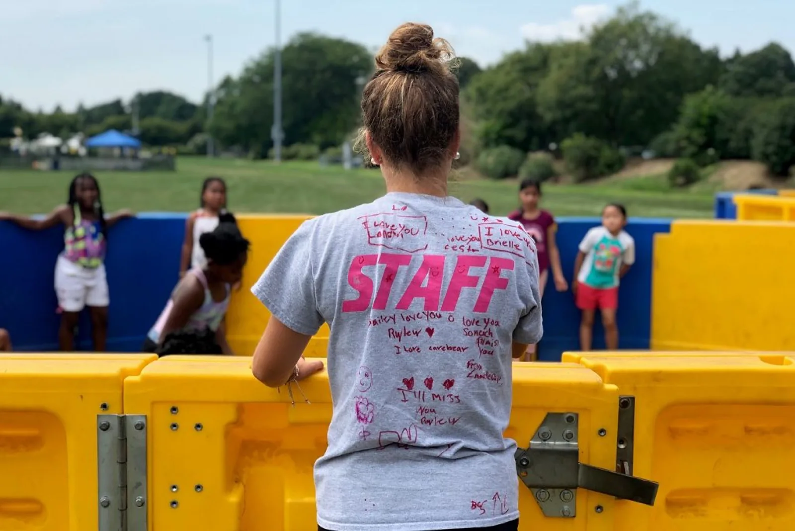 A summer camp counselor in a signed STAFF shirt watching kids play