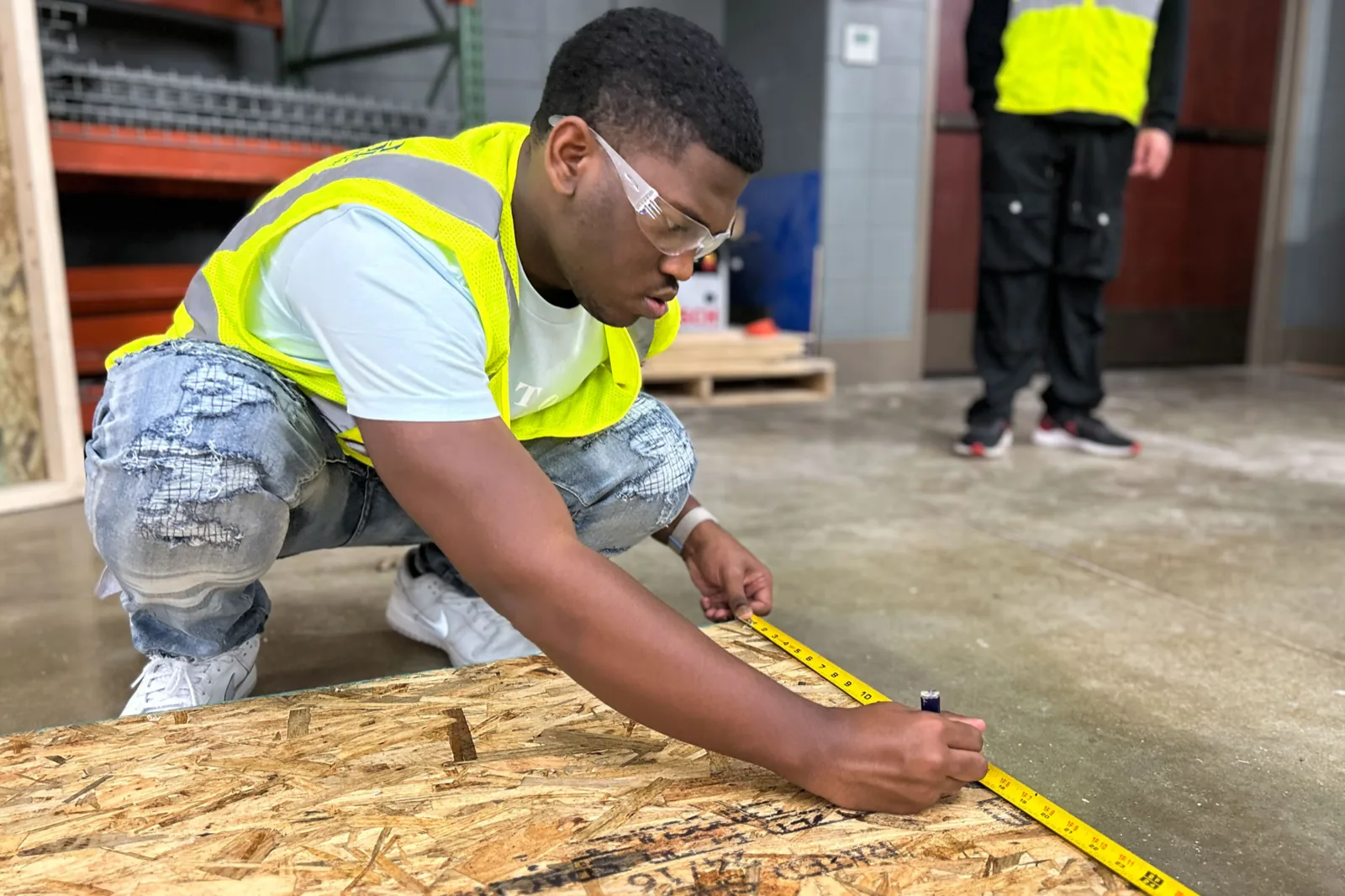 A young man in a hi-vis vest measuring wood on a construction site