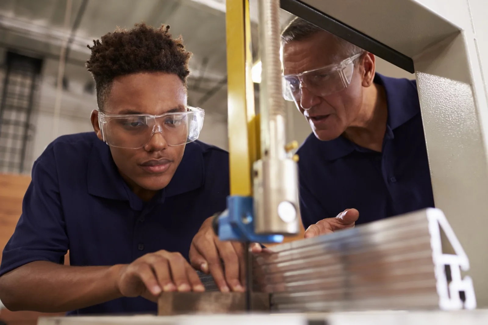 A young man and a mentor operating a band saw in a workshop