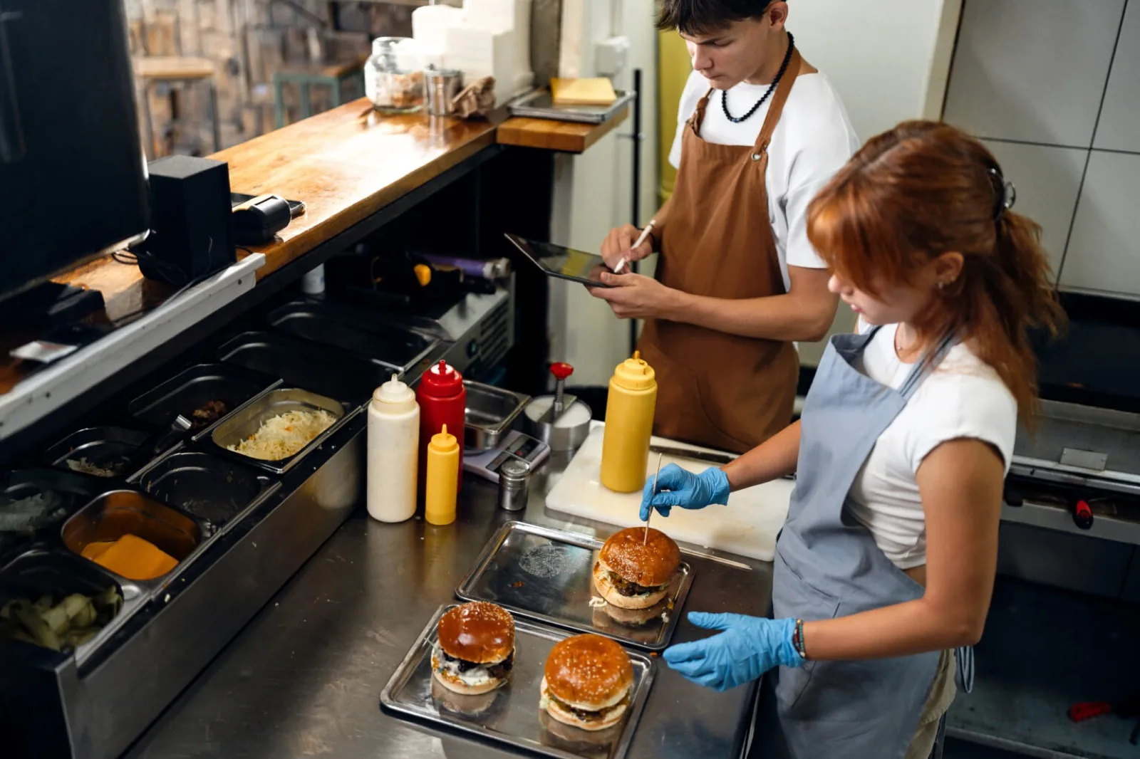 Two teens in aprons assembling burgers in a restaurant kitchen